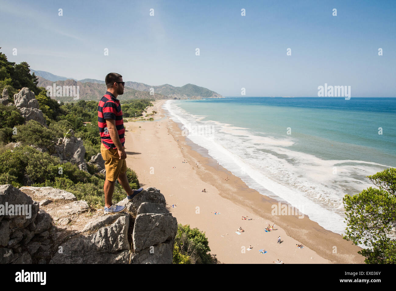Man on top of cliff looking out over Olympos beach, Lycian way, Turkey Stock Photo