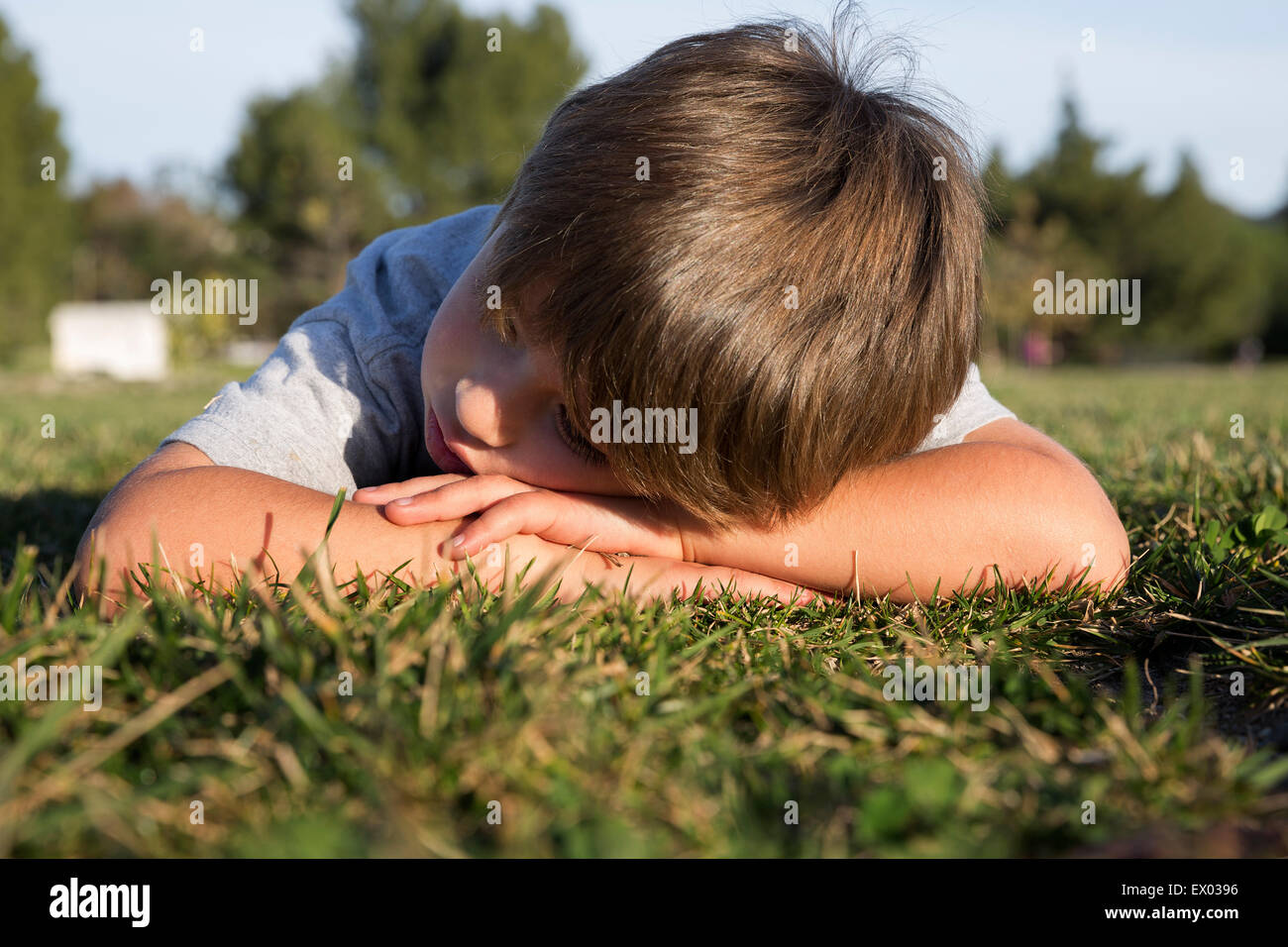 Sullen boy with head down lying on park grass Stock Photo