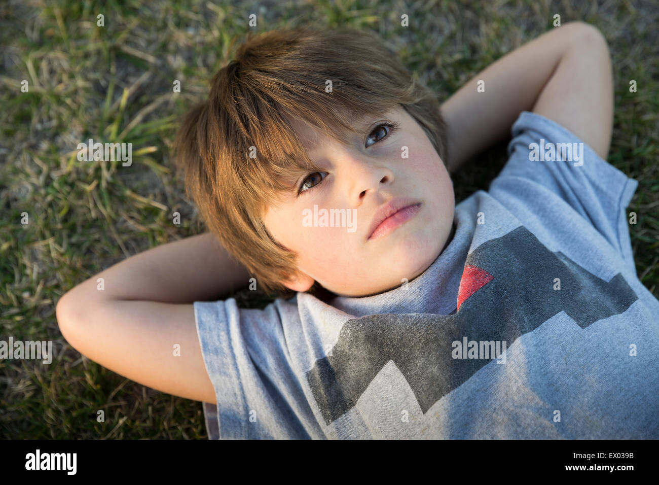 Portrait of boy lying on park grass gazing up Stock Photo