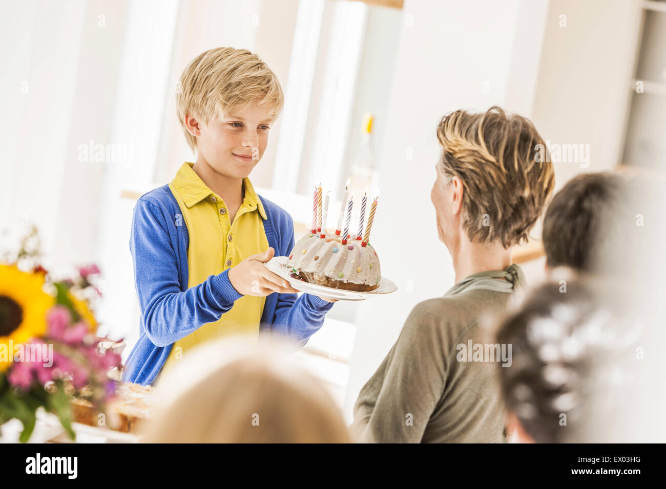Boy handing grandmother birthday cake at party in dining room Stock Photo