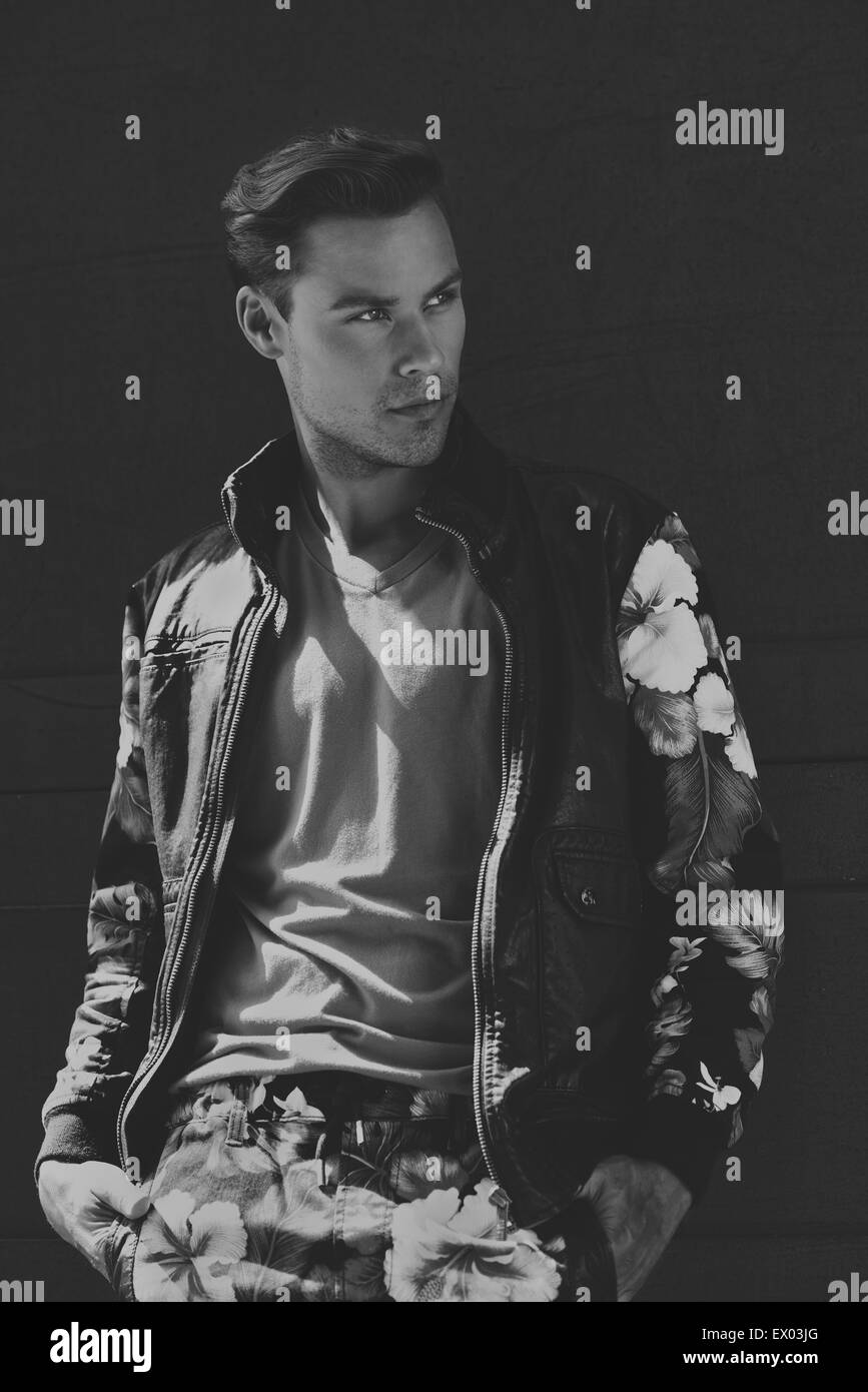 A Caucasian man, male model black and white portrait. He wears a floral leather jacket and lean against a wall, looking relaxed. Stock Photo