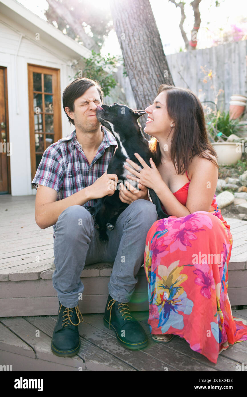 Young couple sitting on patio with dog licking face Stock Photo