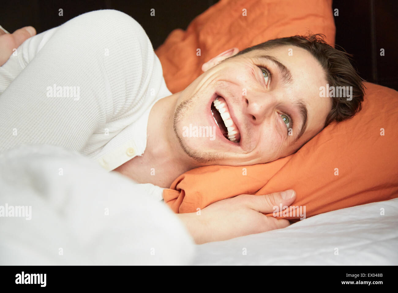 Close up of young man lying in bed and laughing Stock Photo