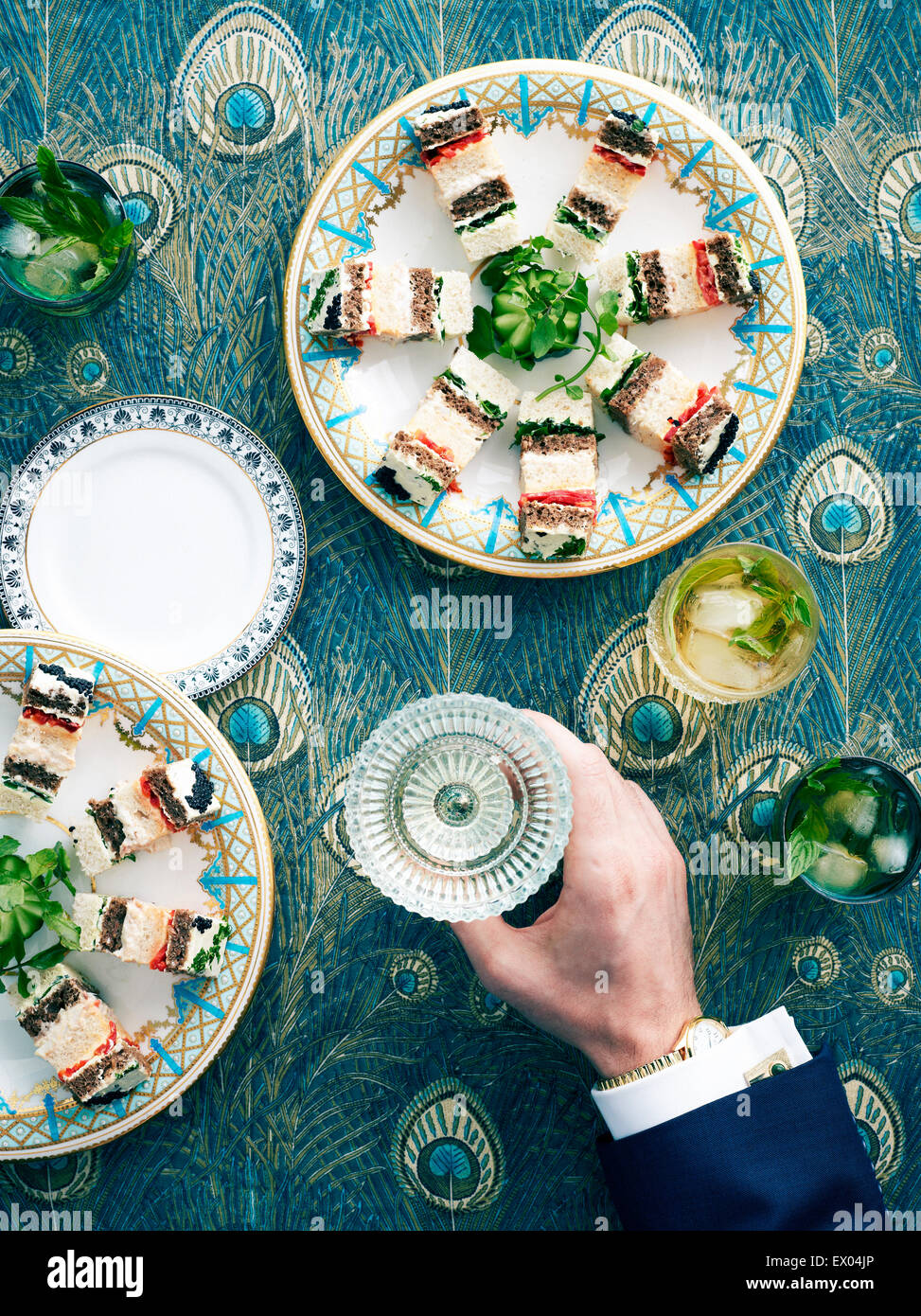 Overhead view of retro styled table with layered ribbon sandwiches and mans hand holding wine glass Stock Photo