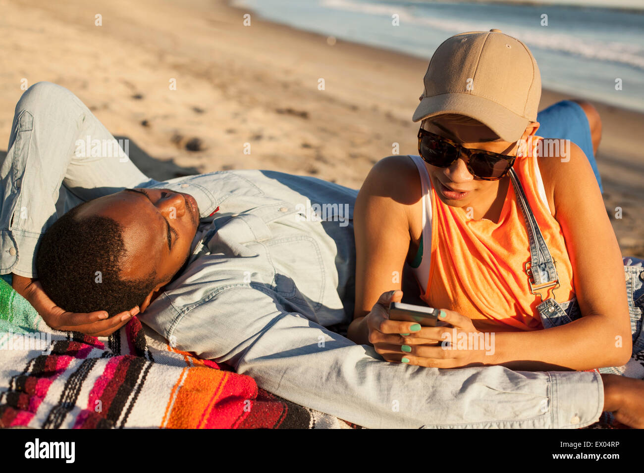 Young couple lying together on beach, woman looking at smartphone Stock Photo
