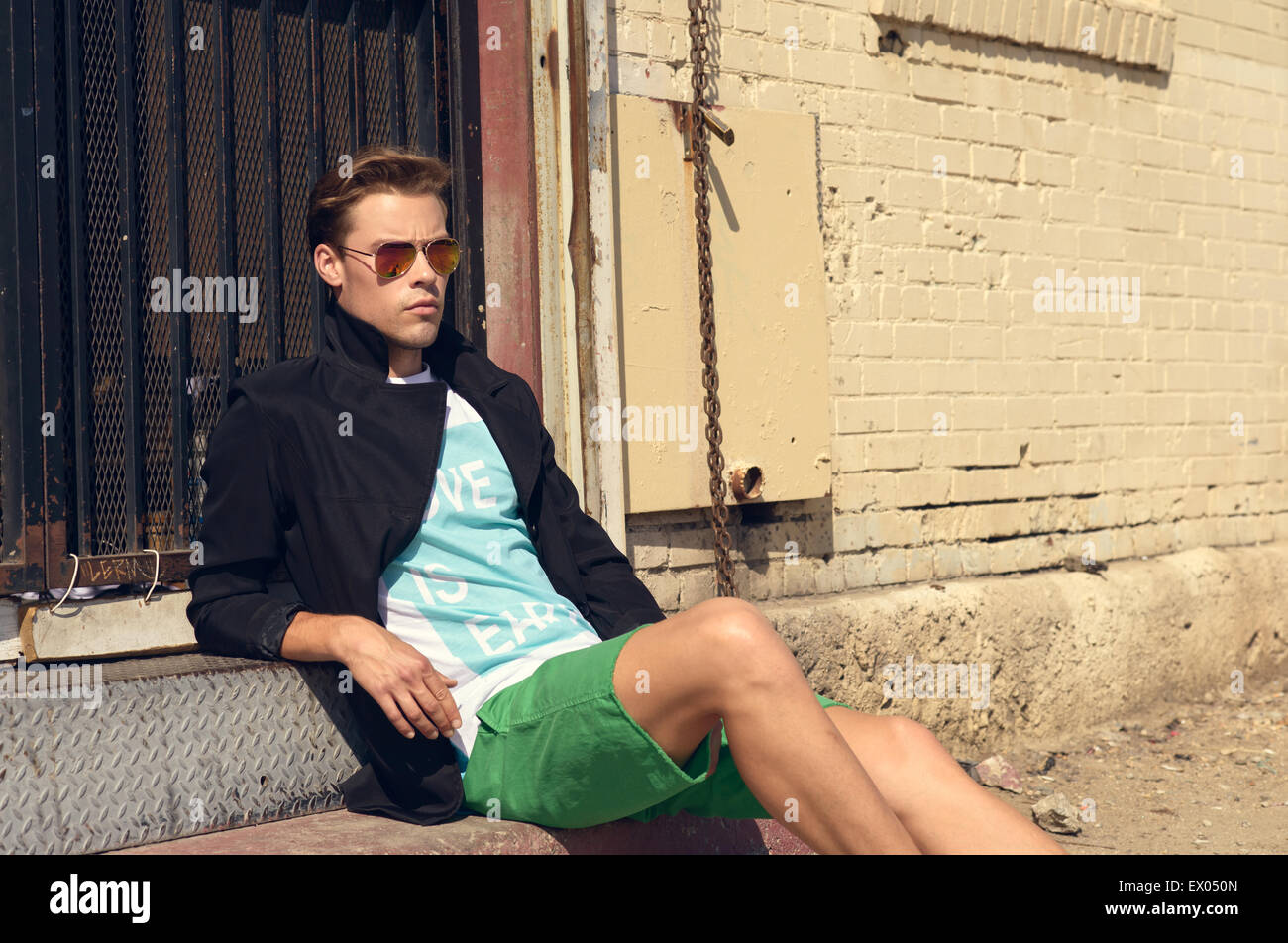 A Caucasian man, male model wearing sunglasses, sitting on a staircase step, leaning back and relaxing. A men's fashion editorial concept. Stock Photo