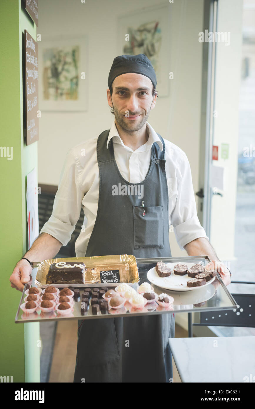 Waiter carrying tray of cakes and cookies in cafe Stock Photo
