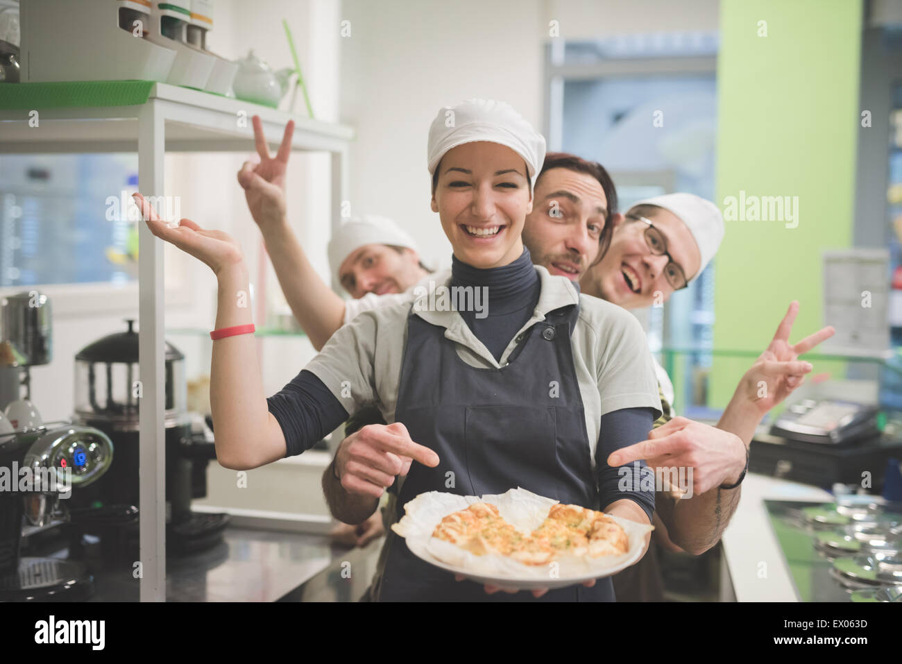 Waitress carrying plate of food, colleagues making fun behind Stock