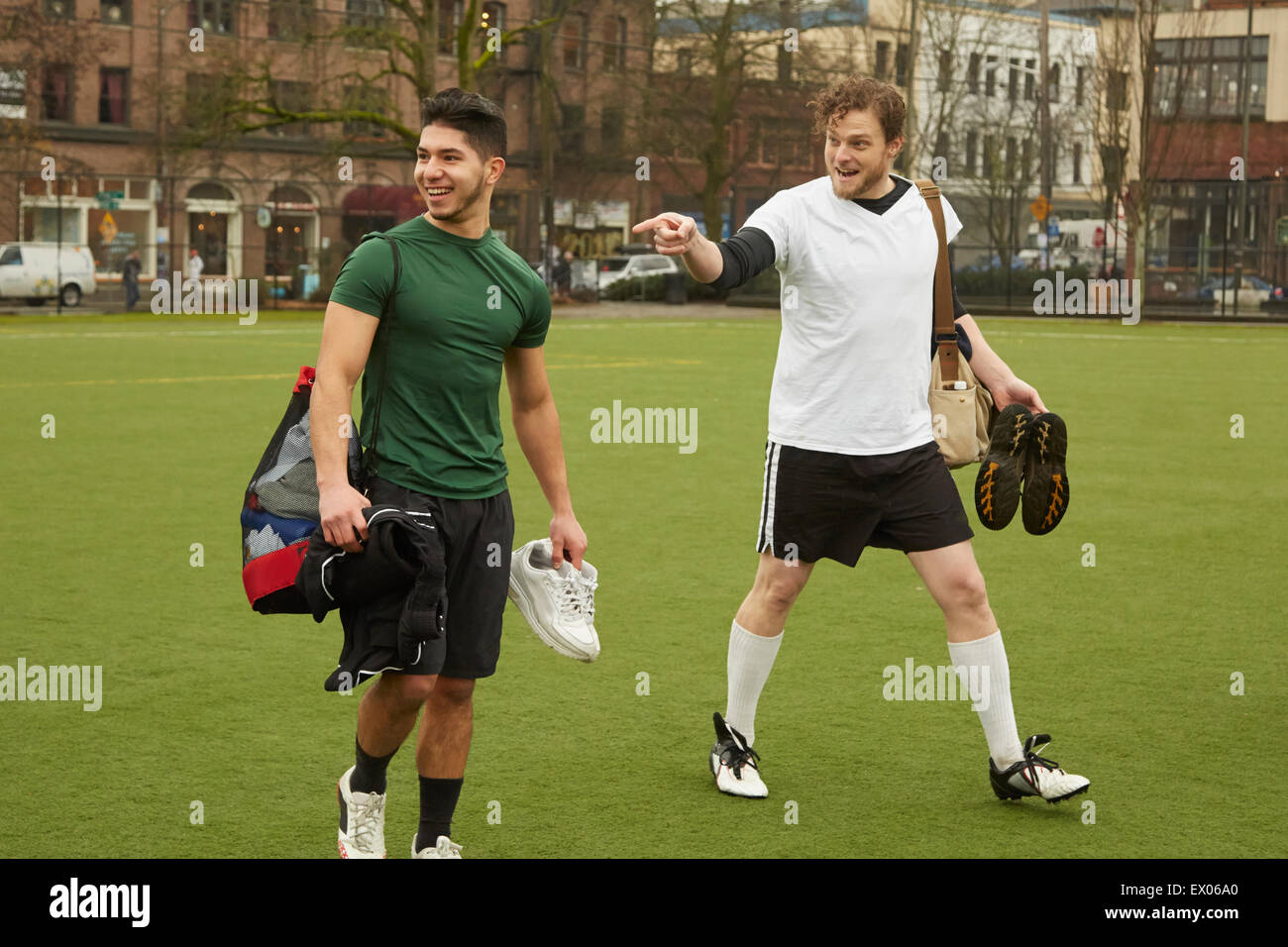 Two male soccer players carrying gym bags on soccer pitch Stock Photo