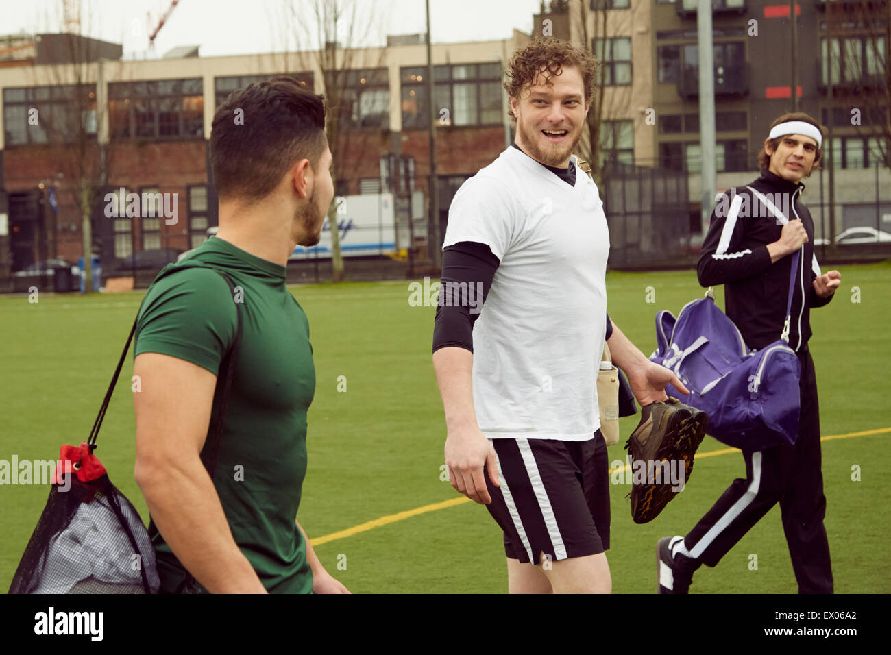 Three male soccer players carrying gym bags on soccer pitch Stock Photo