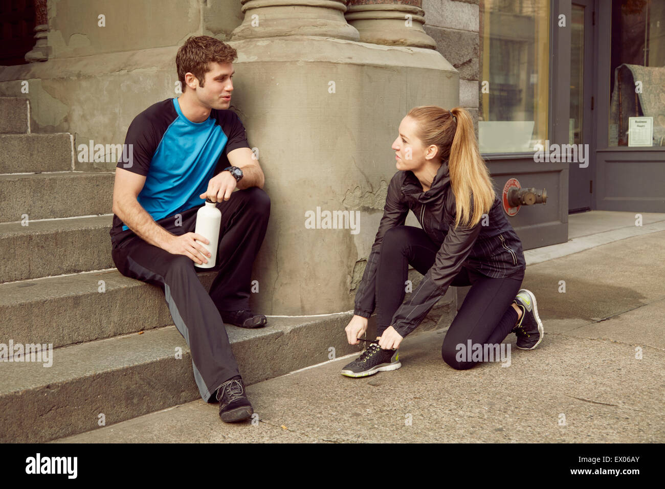 Young male and female runners preparing for run on sidewalk Stock Photo