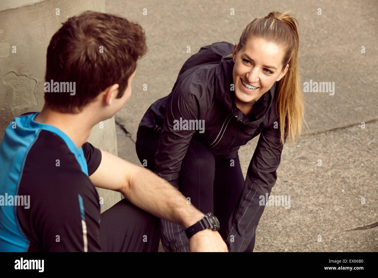 Young male and female runners tying shoelace on sidewalk Stock Photo
