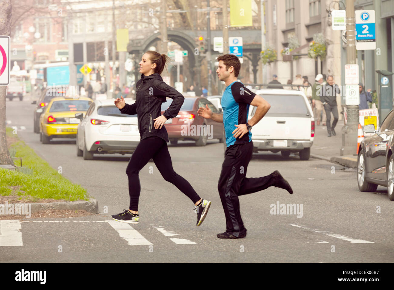 Young man and woman running across city road Stock Photo