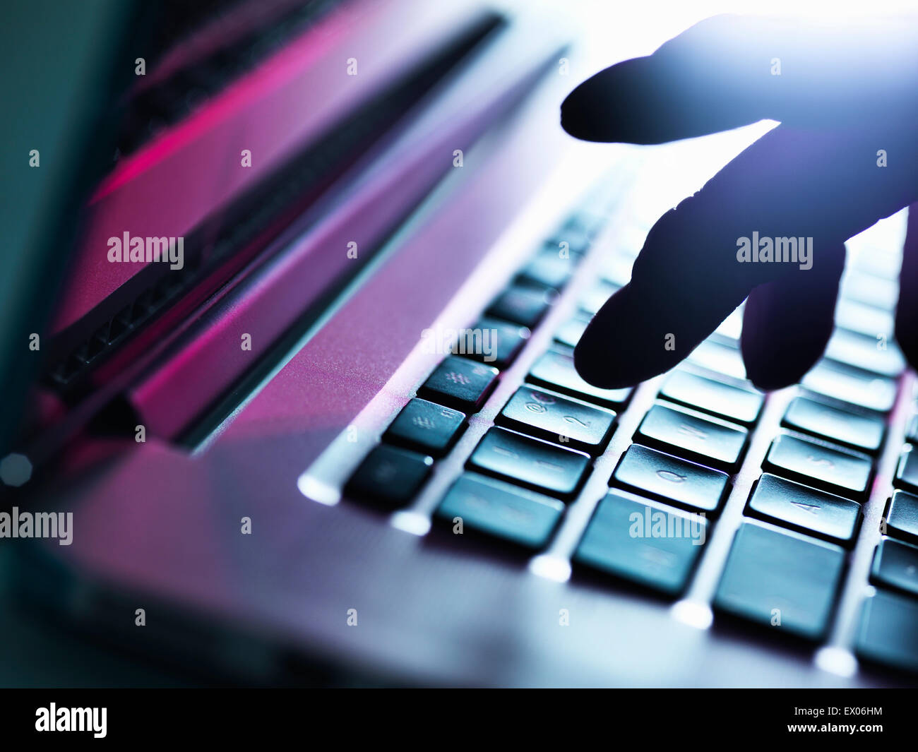 Close up of silhouetted male hand typing on laptop keyboard Stock Photo