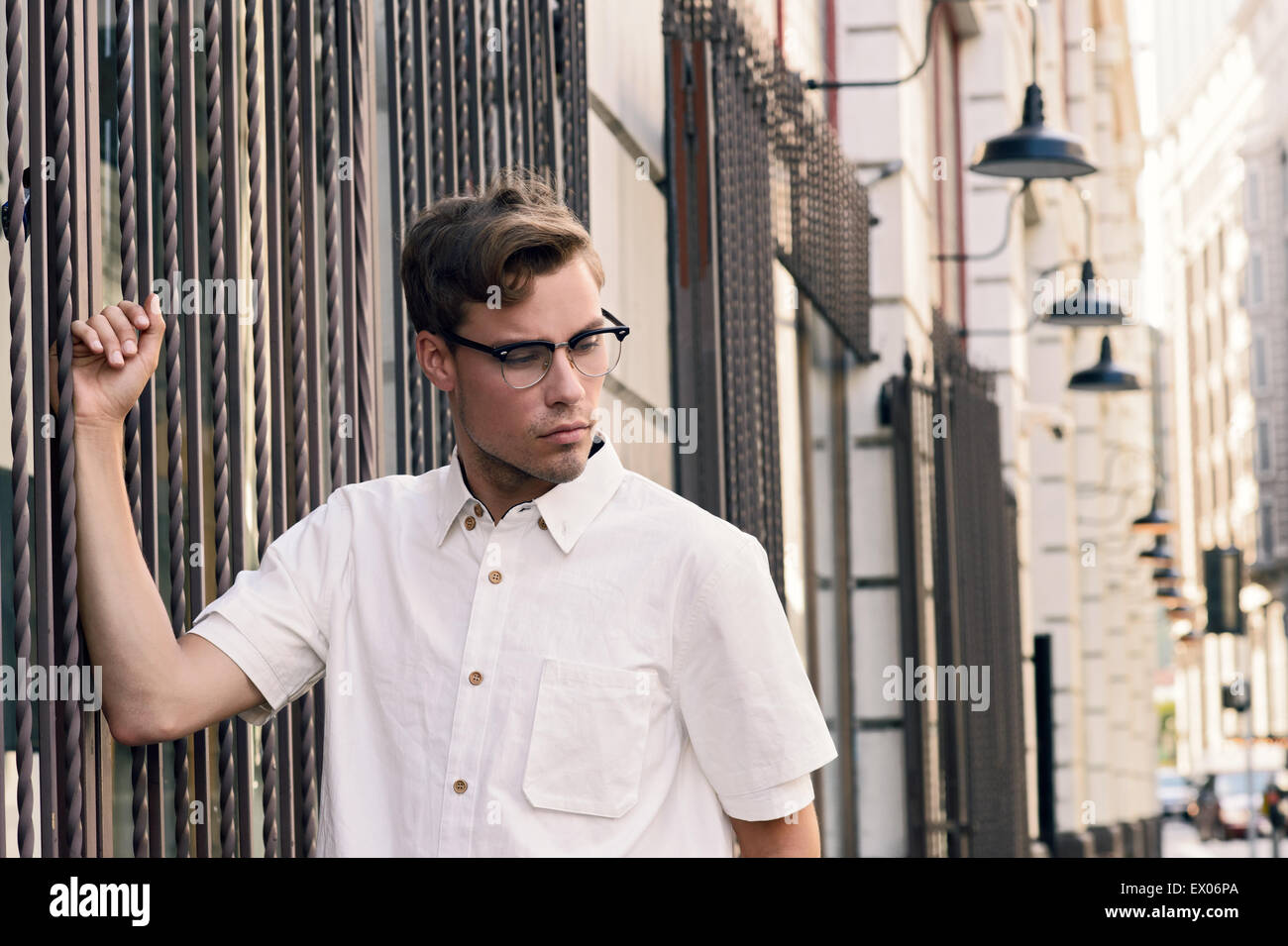 A Caucasian man, male model standing on a street with vintage city background.He wears vintage eye glasses. A vintage inspired men's fashion concept. Stock Photo