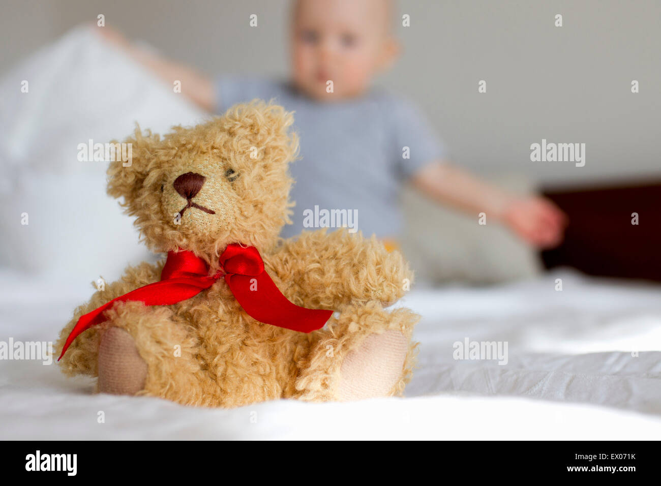 Cute teddy bear sitting up in bed in front of baby girl Stock Photo - Alamy