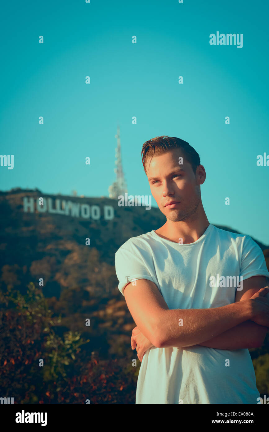 A vintage portrait of a young man, male model, posing in a white t-shirt with the Hollywood Sign in the background. A 50s retro fashion concept. Stock Photo