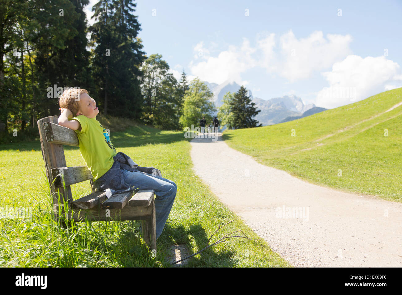 Boy sitting on park bench at rural roadside,  Eckbauer bei Garmisch, Bavaria, Germany Stock Photo