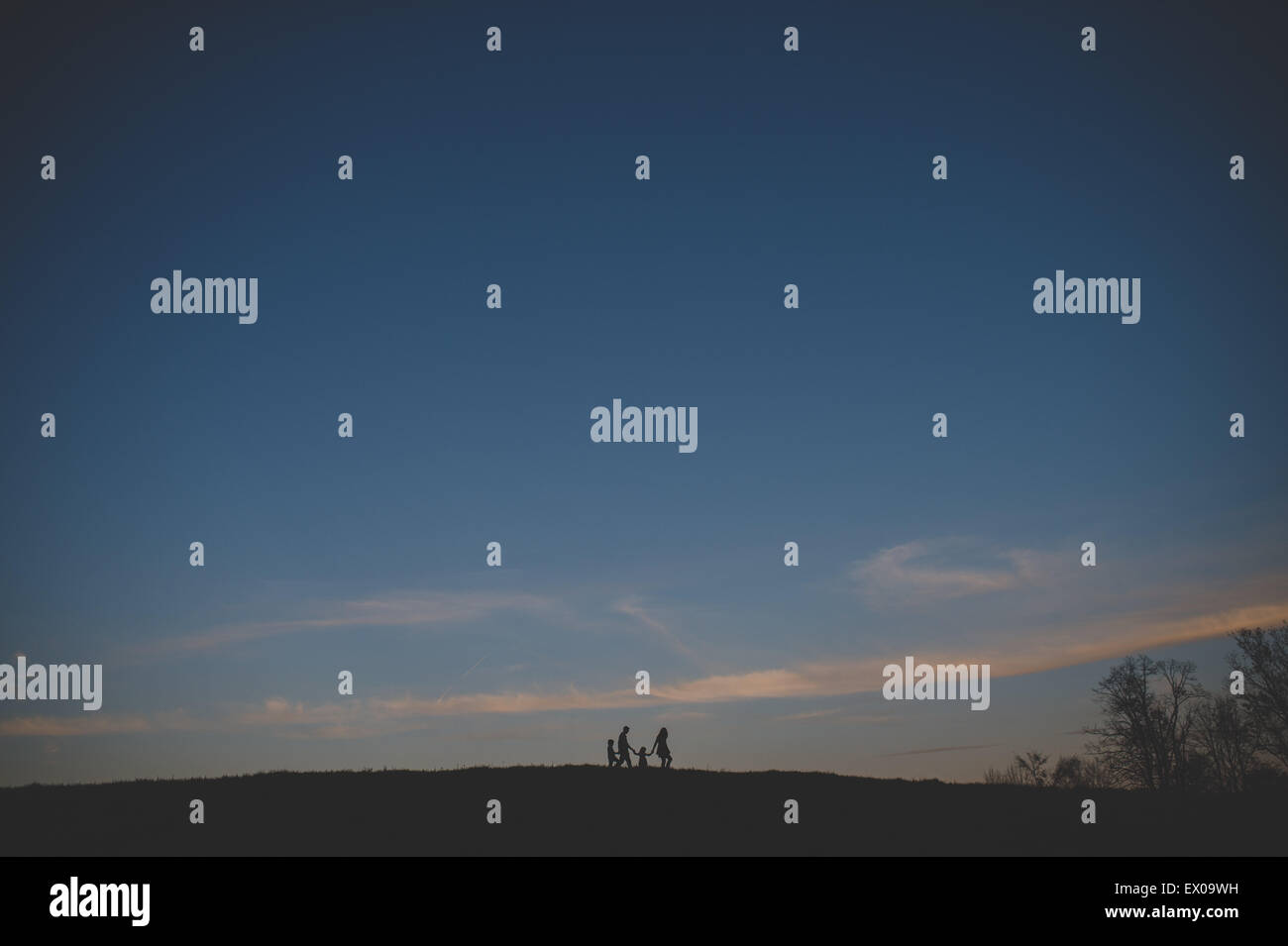 Silhouetted view of parents with son and daughter strolling on hill at dusk Stock Photo