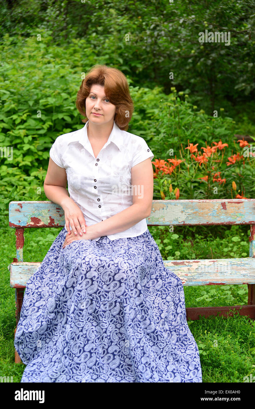 An adult woman sitting on a bench in the garden Stock Photo