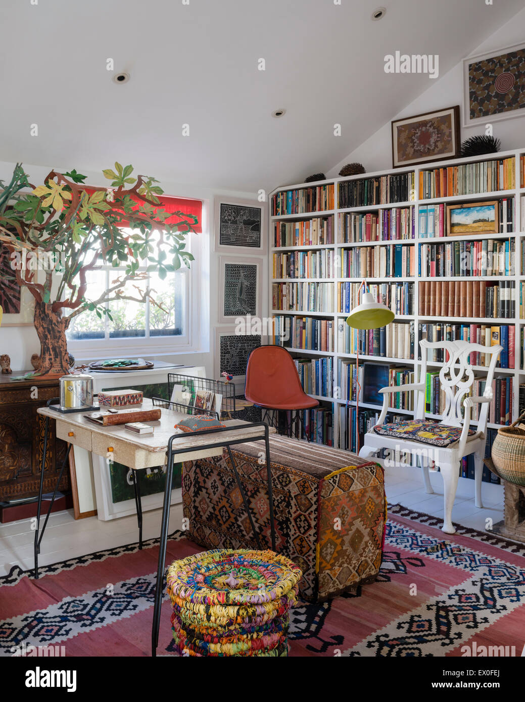 Inbuilt book shelving in living room with uzbek rug, kilim covered bench and aboriginal wall art Stock Photo