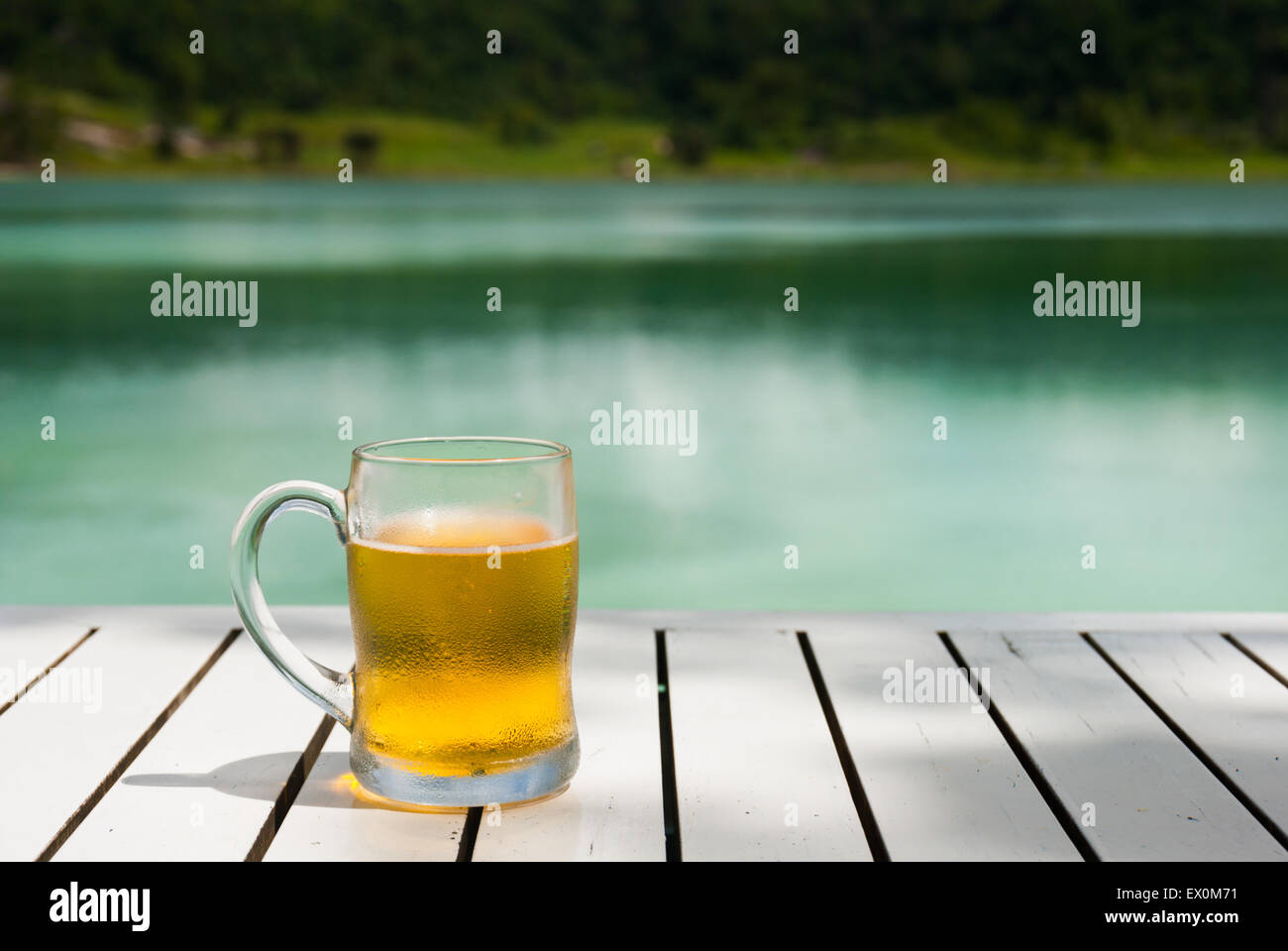 Glass of beer on wooden table of lakeside restaurant. Stock Photo