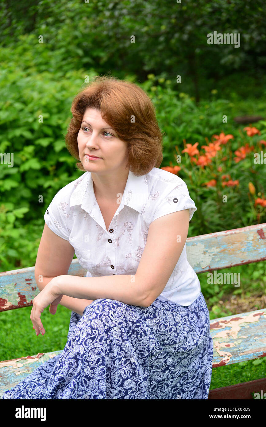 An adult woman sitting on a bench in the garden Stock Photo