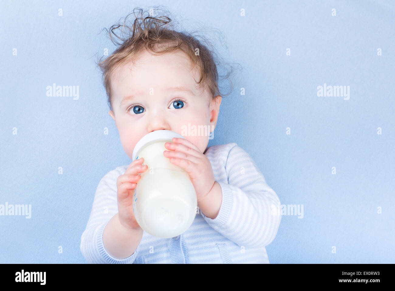 Sweet little baby with beautiful blue eyes drinking milk in a plastic bottle relaxing on a blue knitted blanket Stock Photo