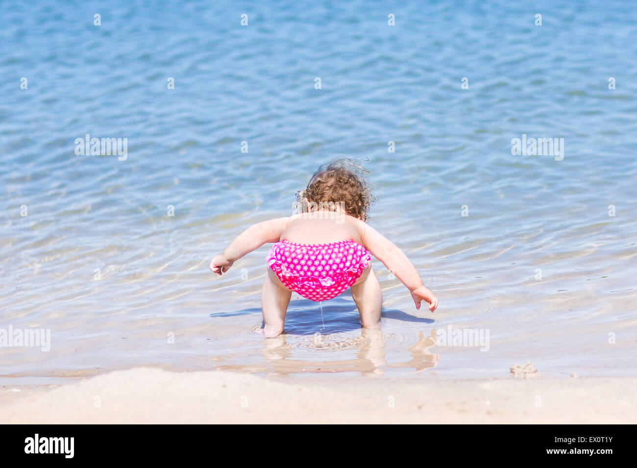 Funny baby girl drinking water on a beautiful beach with clear blue water  Stock Photo - Alamy