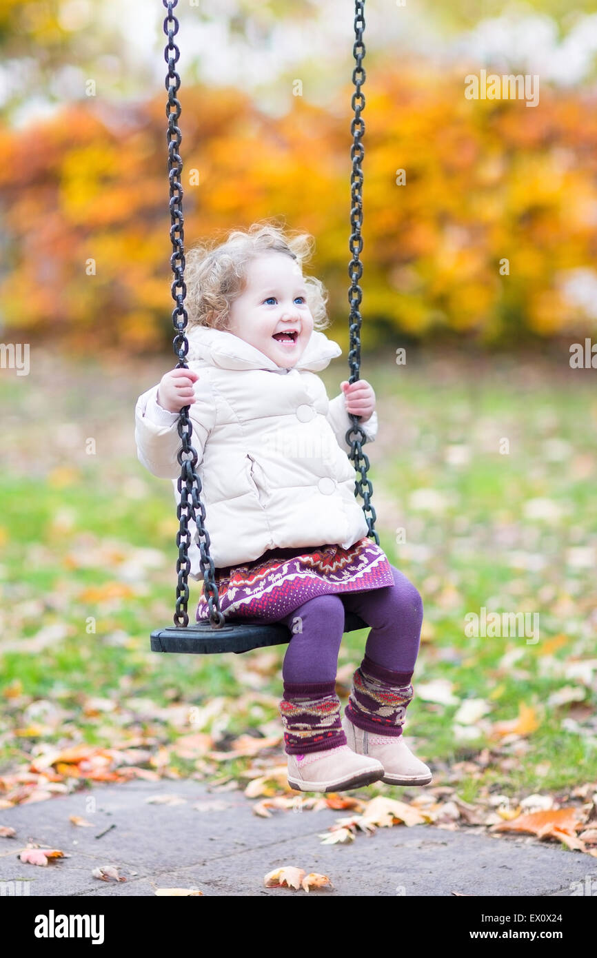 Happy laughing toddler girl playing on a swing with golden autumn trees in the background Stock Photo