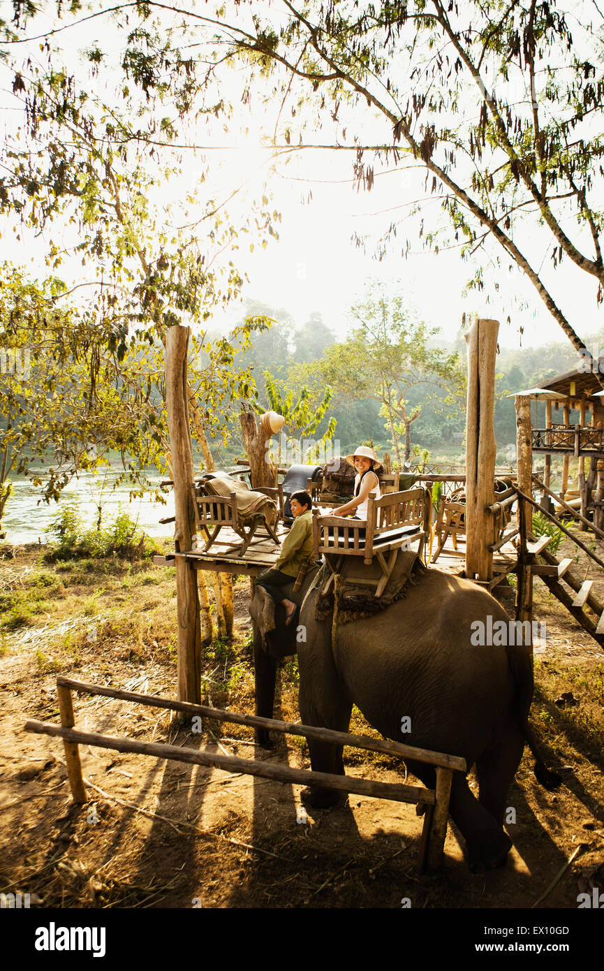 A Lao woman and mahout ride an elephant on the Khan River. Luang Prabang, Laos. Stock Photo