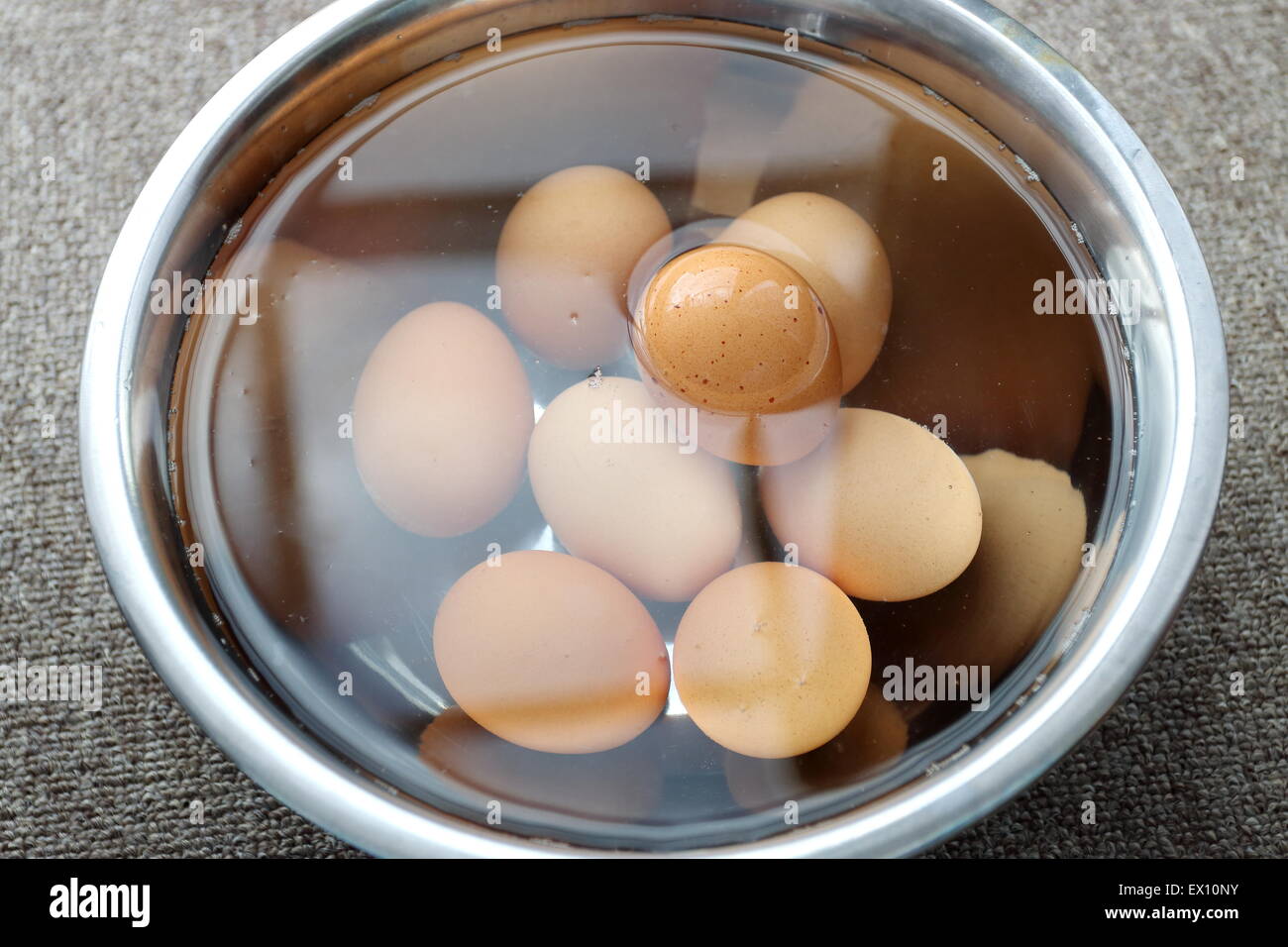 Soaking brown eggs in stainless steel bowl of water Stock Photo