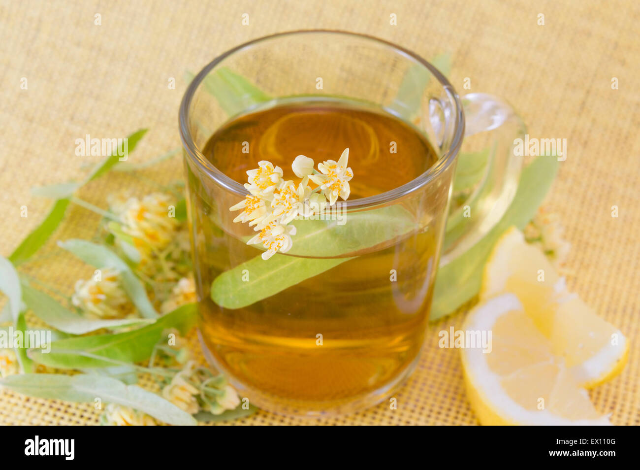 Cup of lime tee with lemon decorated with lime flower on yellow tablecloth Stock Photo