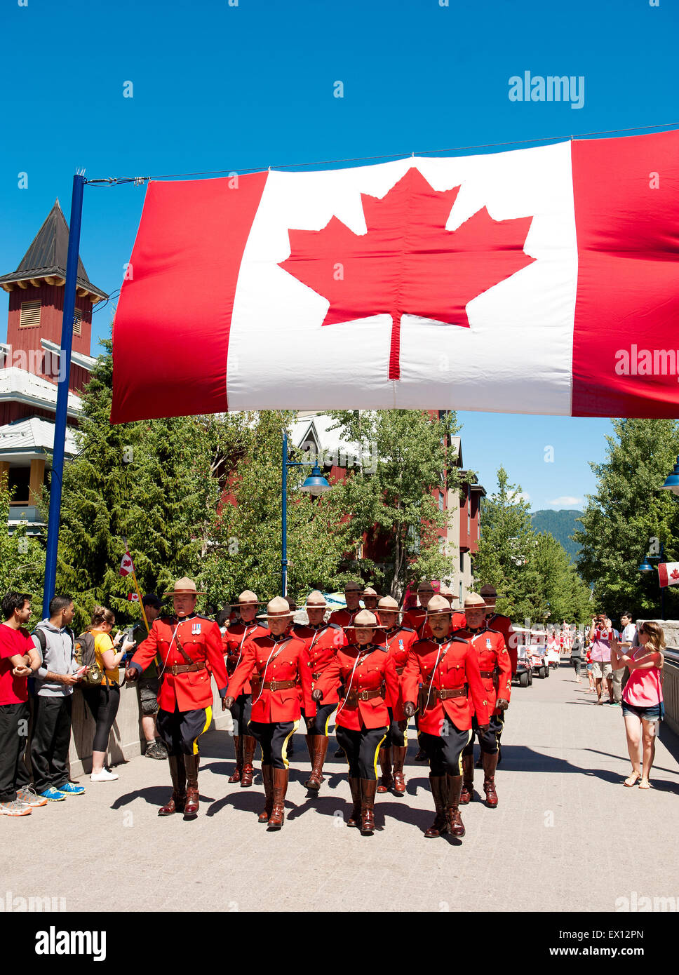 Royal Canadian Mounted Police officers parade under a Canadian flag in ceremonial red serge uniforms for Canada Day.  Canadian P Stock Photo
