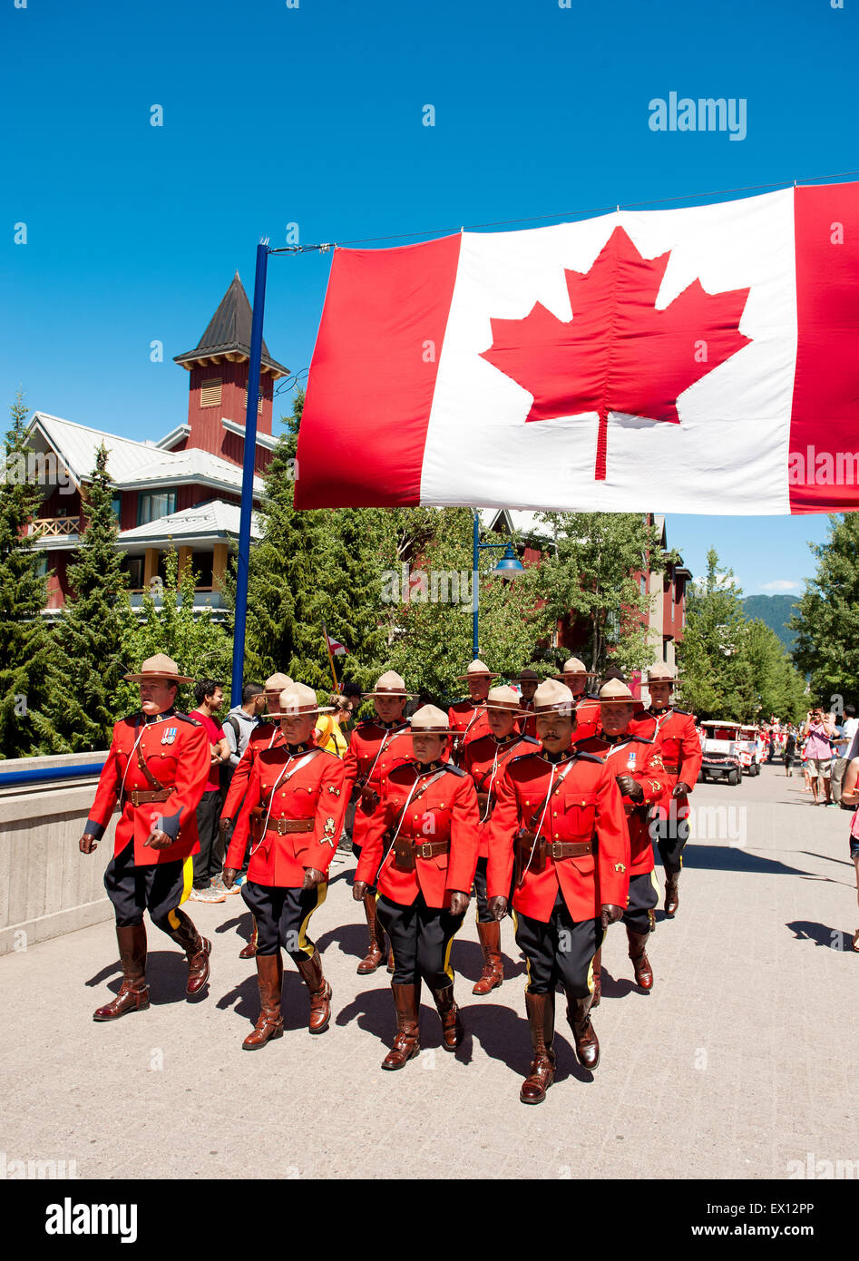 Royal Canadian Mounted Police officers parade under a Canadian flag in ceremonial red serge uniforms for Canada Day.  Canadian P Stock Photo