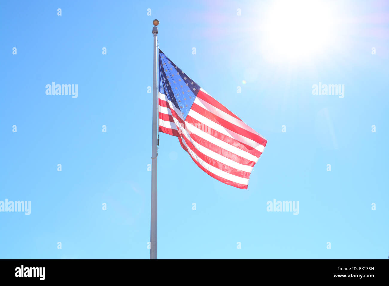 U.S. flag with a blue sky and the sun shining in the background Stock Photo