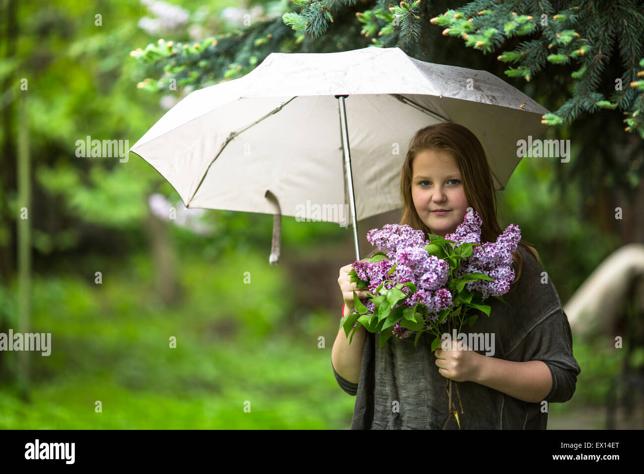 Teen girl with a bouquet of lilacs, standing under an umbrella in the ...