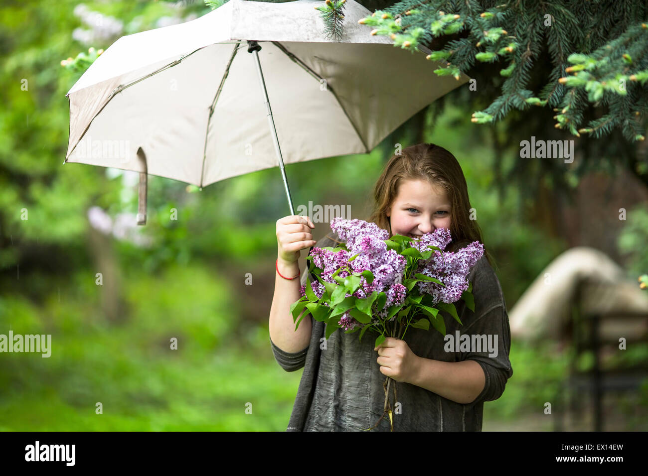 Teen girl with a bouquet of lilacs, standing under an umbrella in the ...