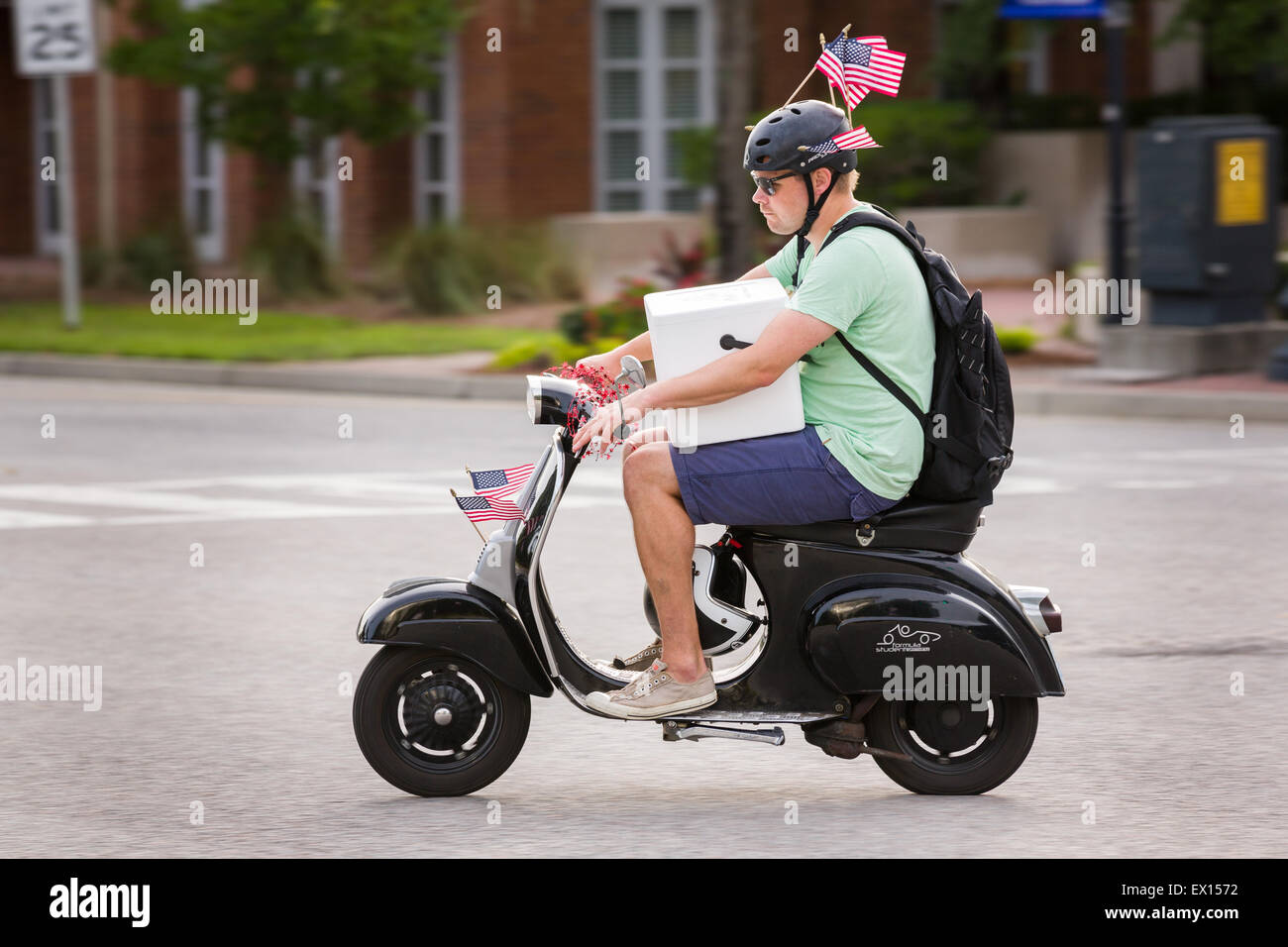 A man carrying a cooler on his scooter rides decorated with American flags during the Daniel Island Independence Day parade July 3, 2015 in Charleston, South Carolina. Stock Photo