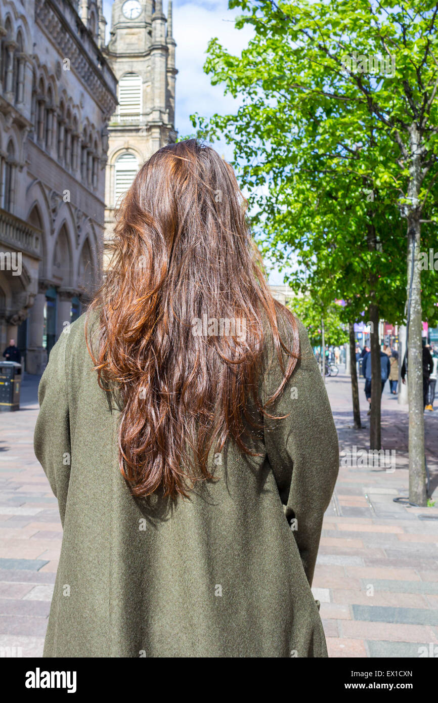 Beautiful, young girl with long brown hair standing with her back to the camera in the streets of big city. Stock Photo