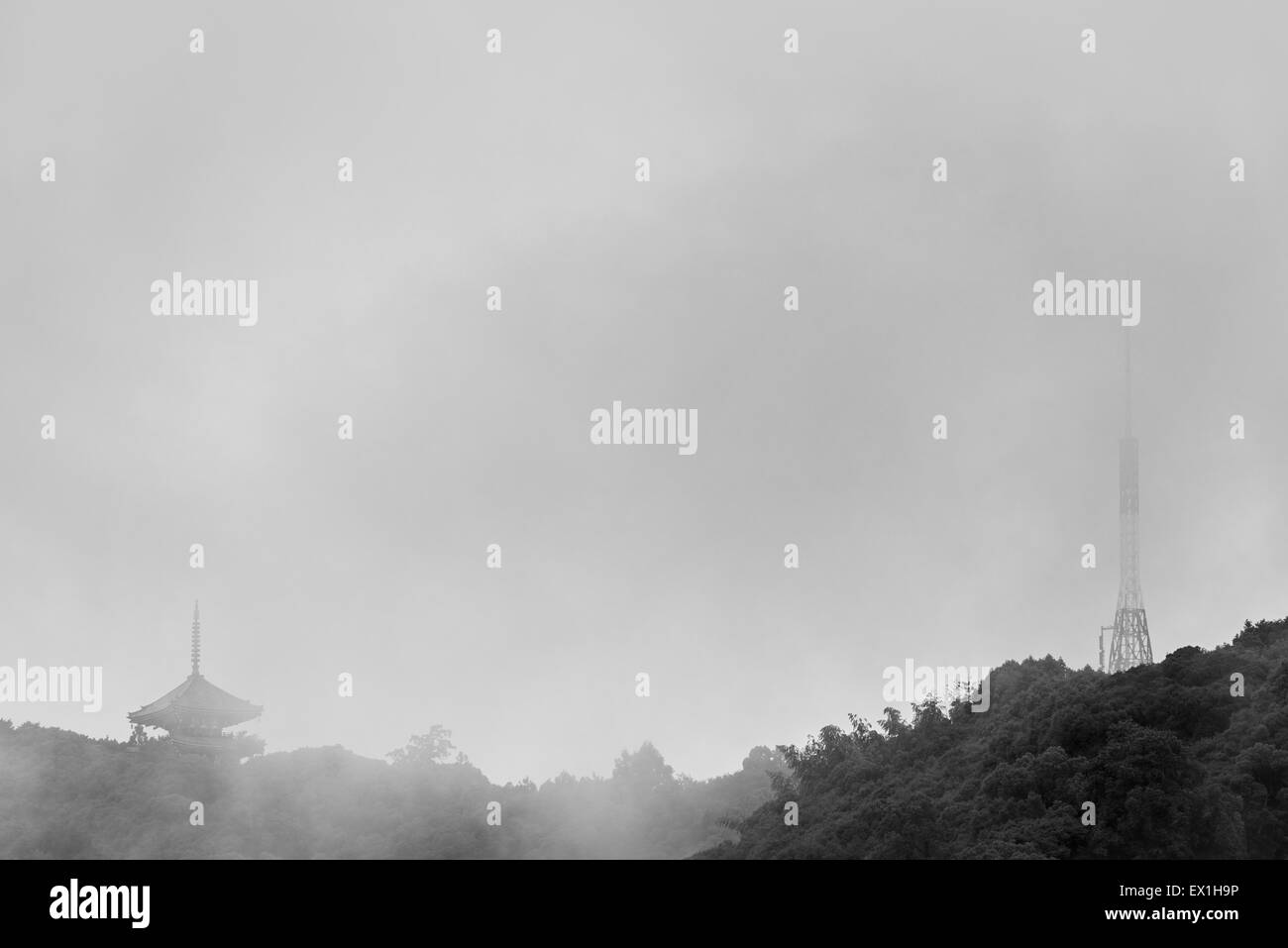 A black and white photo of an old Japanese Pagoda next to a modern radio tower on top of a mountain on a rainy, foggy day. Stock Photo