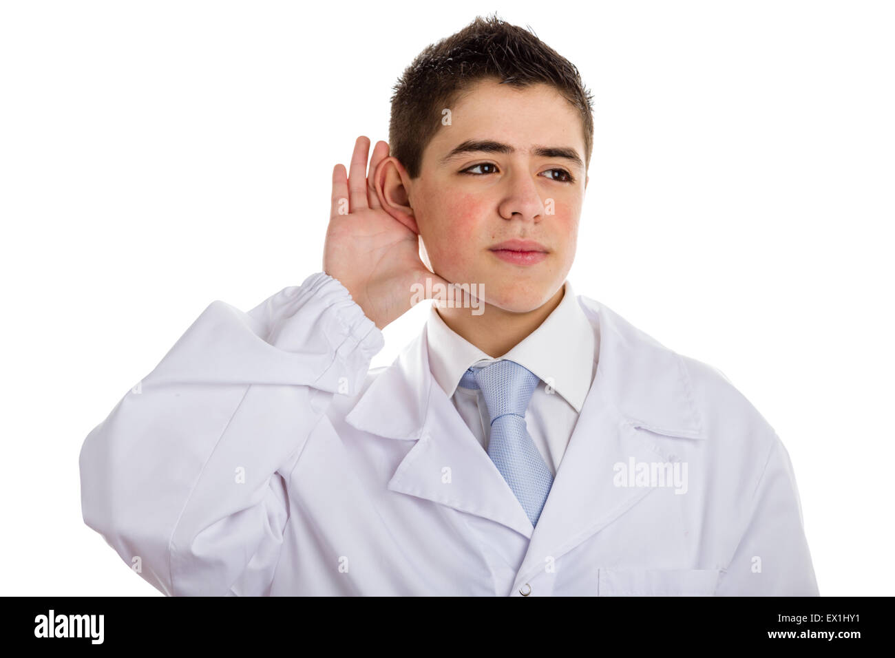 A boy doctor in white coat and blue tie helps to feel medicine more friendly: he is hearing something while holding his ear. His acne skin has not ben retouched Stock Photo