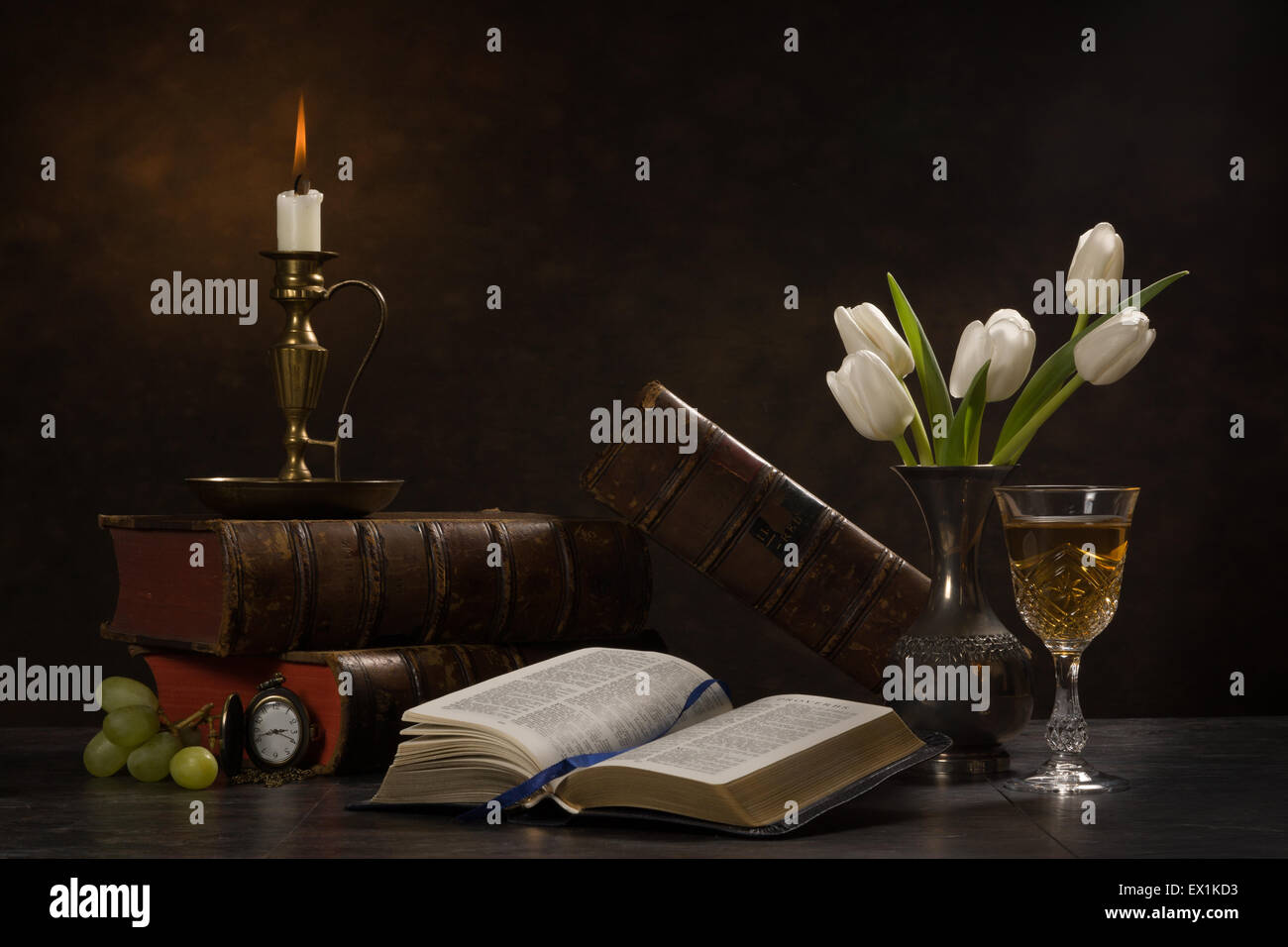 Still life of an open bible surrounded by books, a candle, tulips in a
