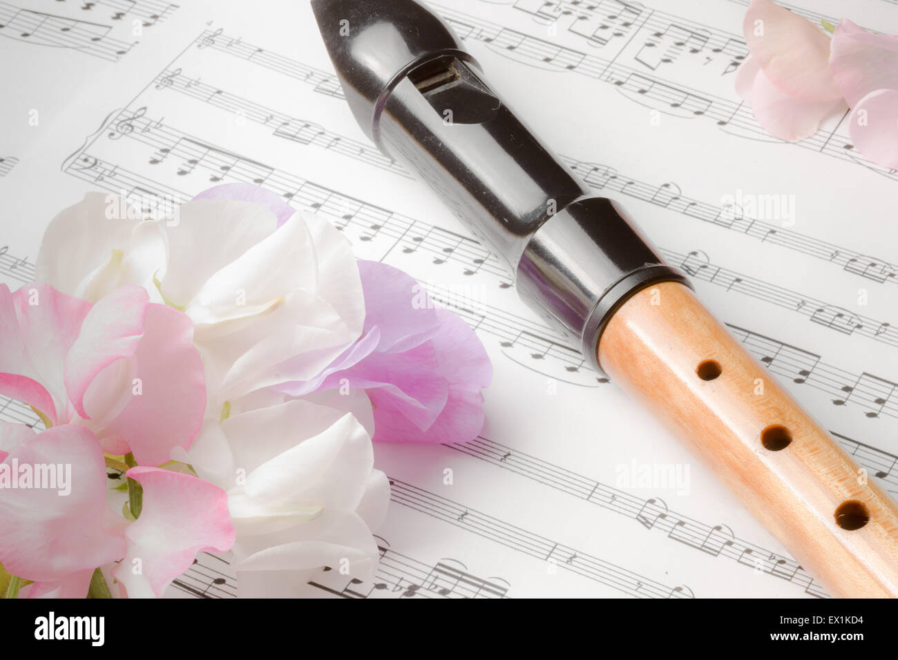 Still life image of a vintage descant recorder placed on sheet music along with sweet pea flowers Stock Photo