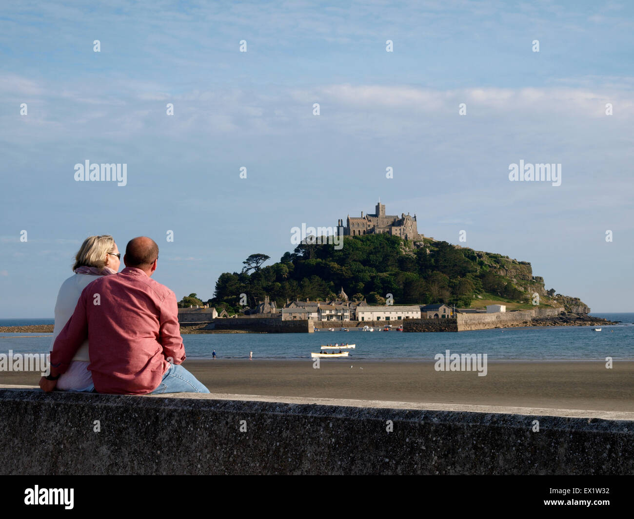 Middle aged couple sat on the seawall overlooking St Michael's Mount, Marazion, Cornwall, UK Stock Photo