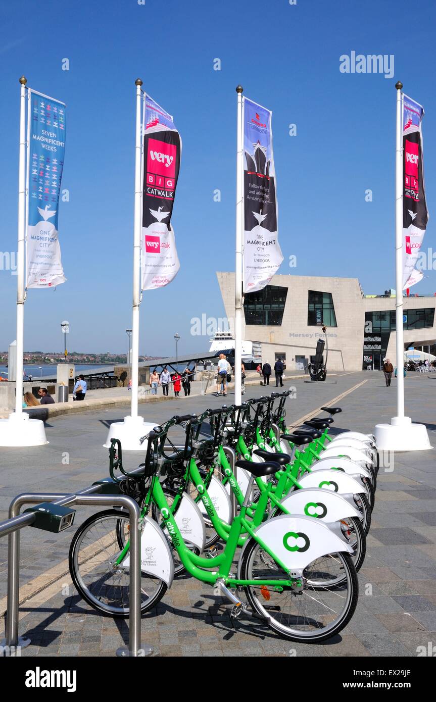 Row of city hire bikes for rent along the waterfront at Pier Head with the Mersey Ferries building to the rear, Liverpool, UK Stock Photo