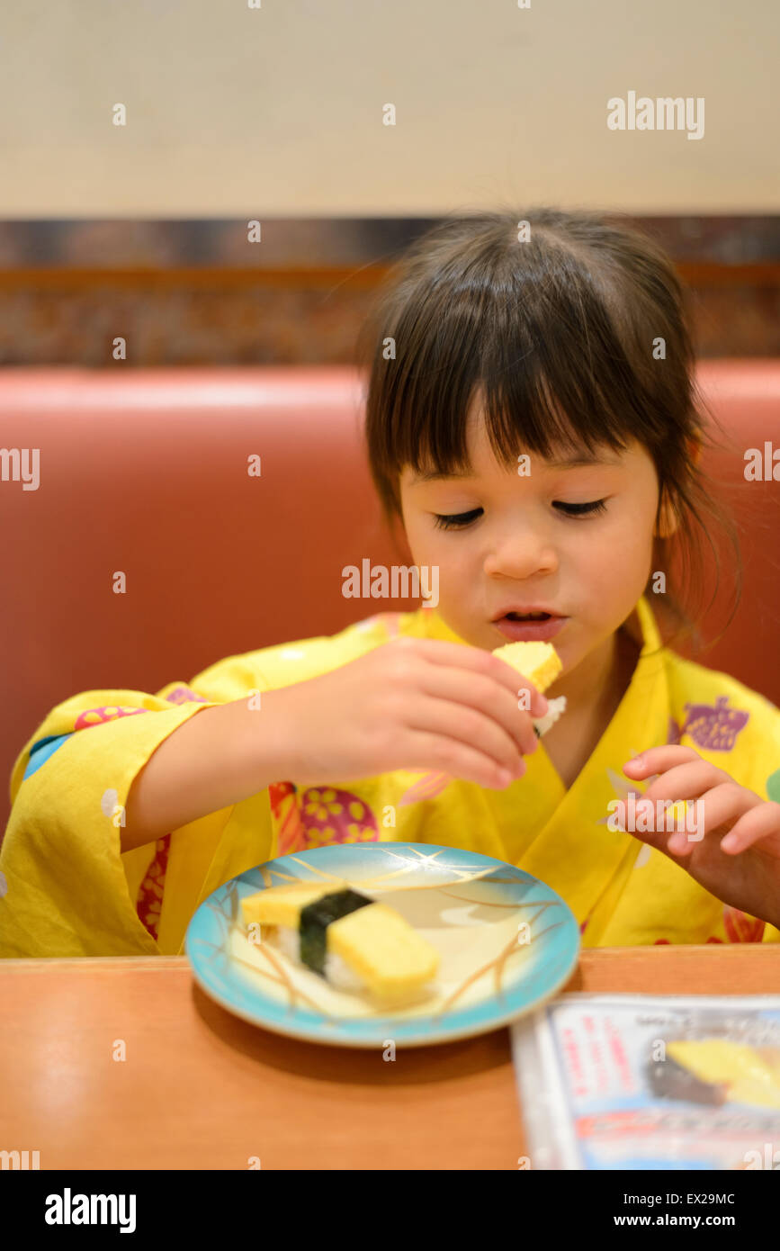 Little girl wearing yukata and eating sushi at a restaurant. Stock Photo