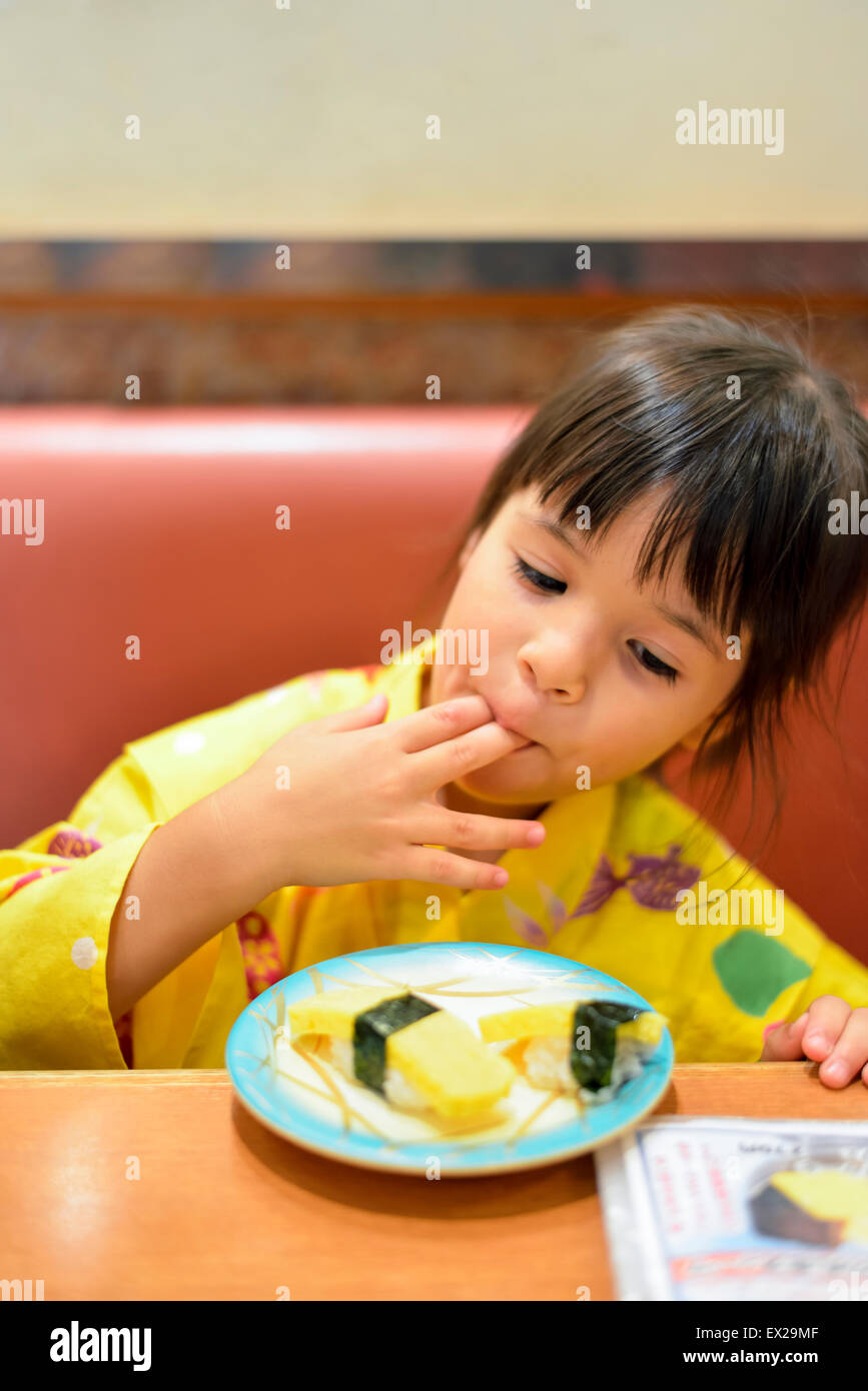 Little girl wearing yukata and eating sushi at a restaurant. Stock Photo