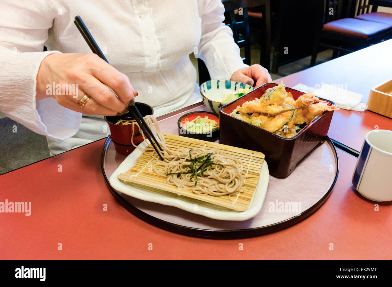 Older woman using chopsticks to eat soba and tempura. Closeup of aged hand holding chopsticks. Stock Photo