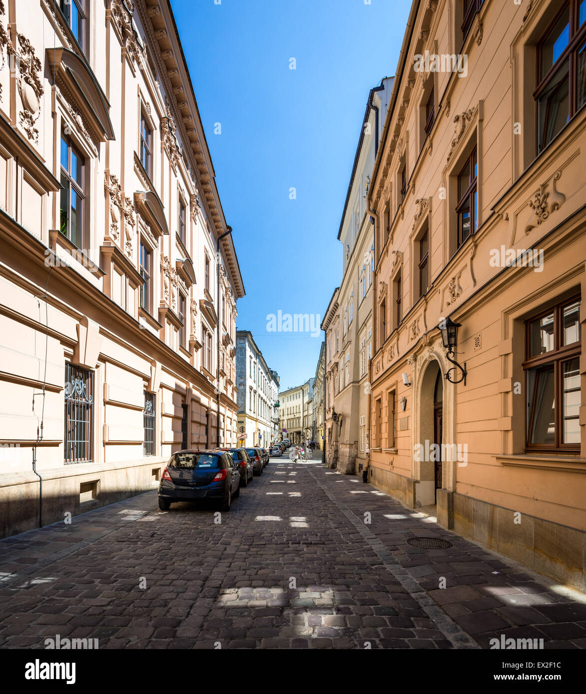 Cars parked near houses in street in Krakow, Poland, Europe. Empty lane in morning. Blue sky and good weather for tourists. Stock Photo